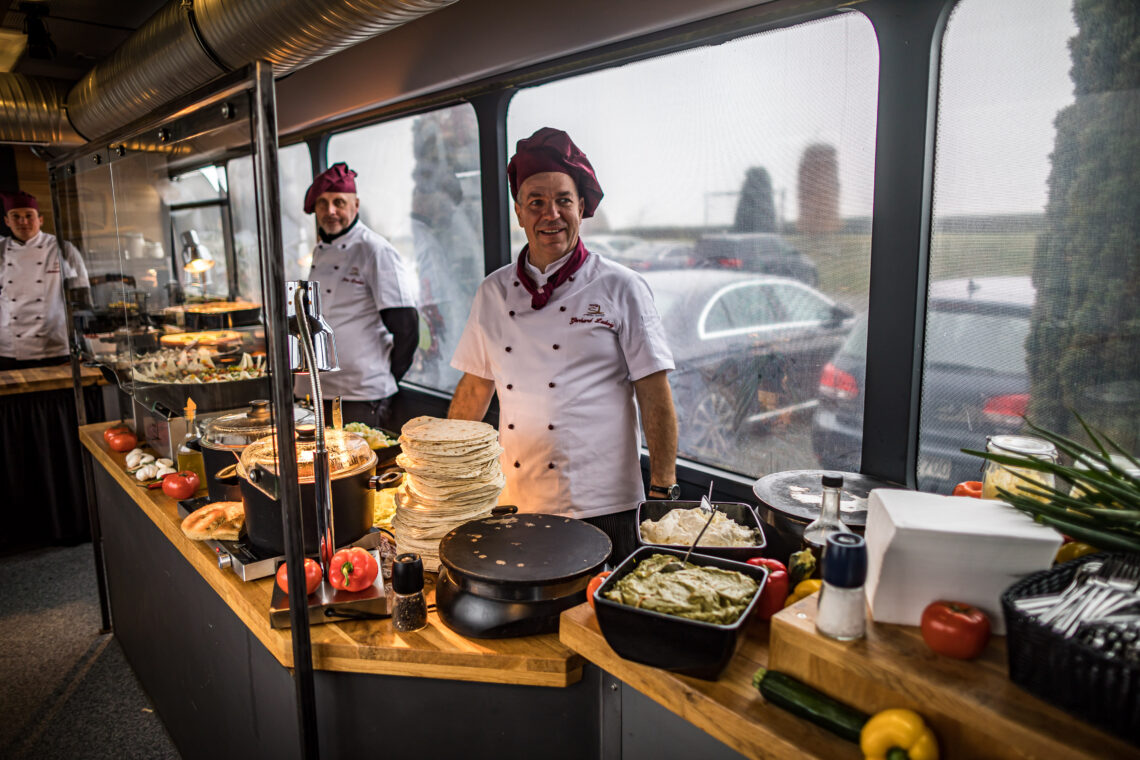 Drei Köche bereiten in einem umgebauten Linienbus Essen zu.
